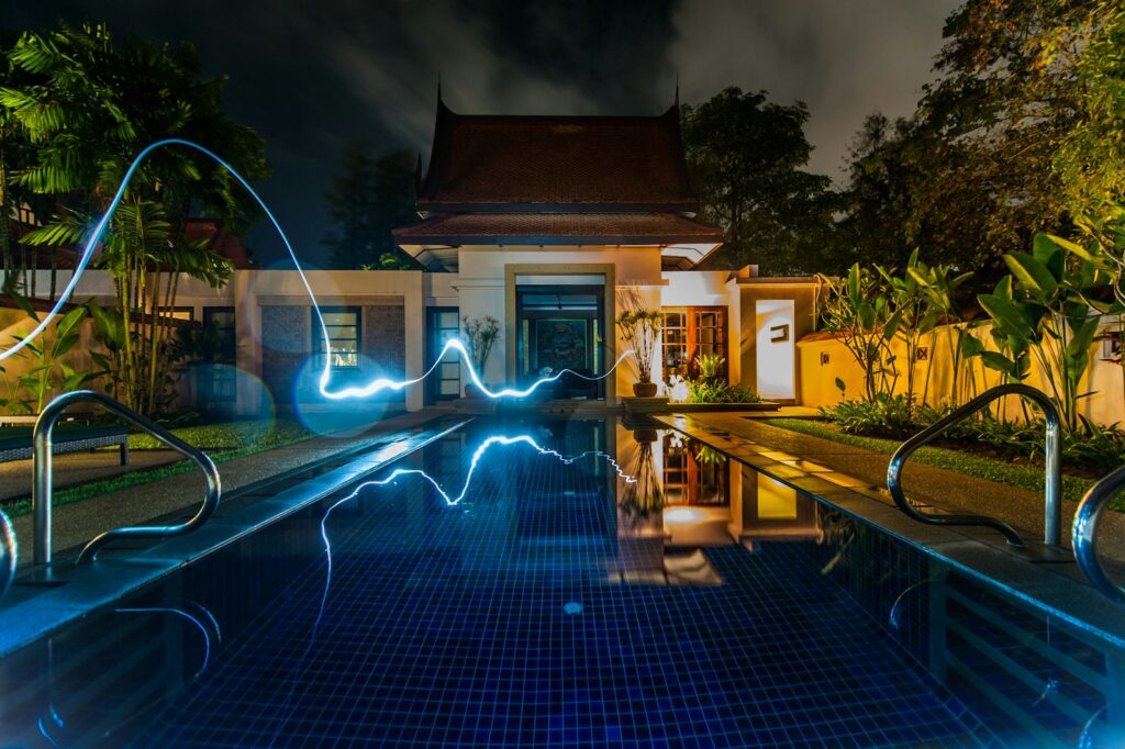 reflection of blue light crossing above pool near house during nighttime